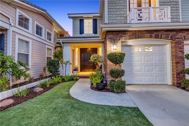 entrance to property featuring an attached garage, brick siding, concrete driveway, a balcony, and a lawn