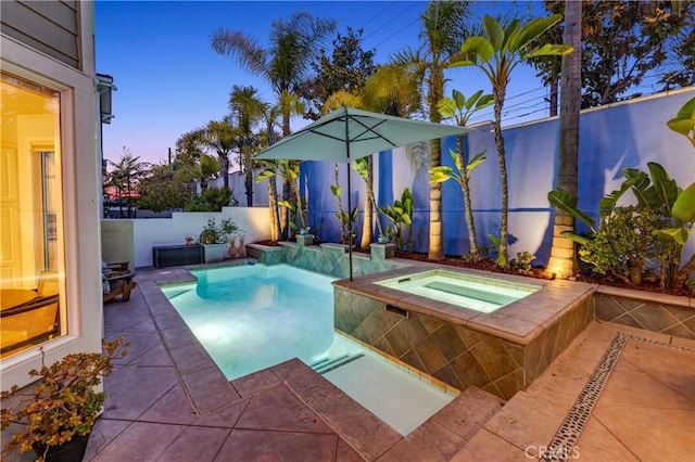 pool at dusk with a fenced backyard, a fenced in pool, an in ground hot tub, and a patio area