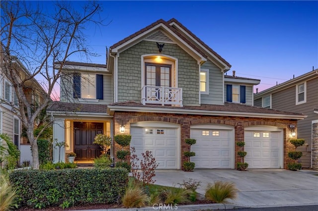 traditional-style house featuring an attached garage, concrete driveway, brick siding, and a balcony