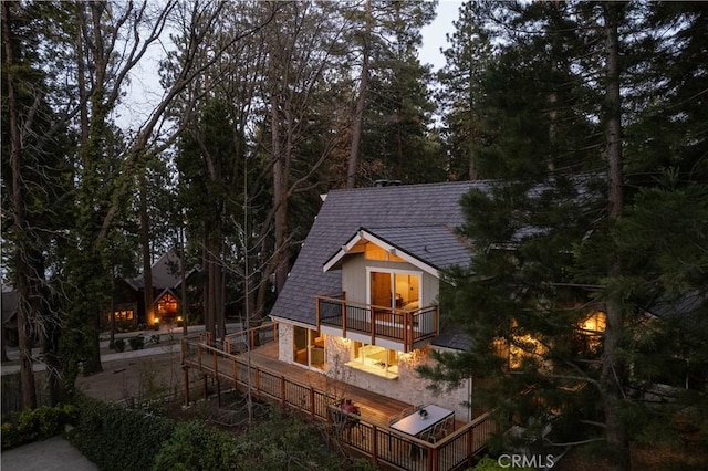 back of property with a shingled roof and a balcony