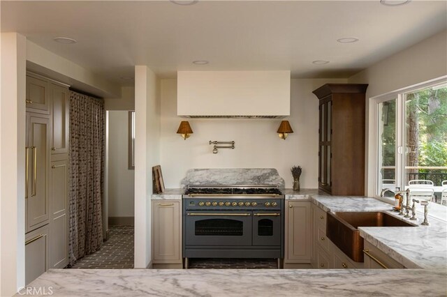 kitchen with baseboards, wall chimney range hood, light stone counters, a sink, and double oven range