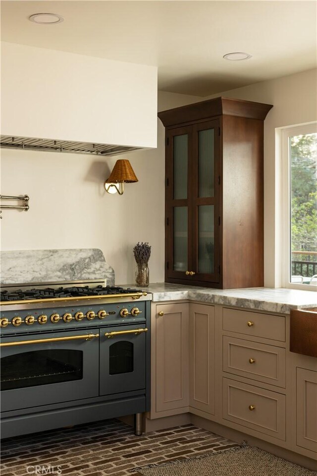 kitchen featuring glass insert cabinets, brick floor, light stone countertops, and double oven range
