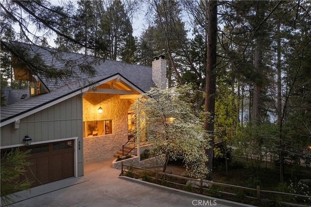 view of front of home with driveway, a chimney, stone siding, and a garage