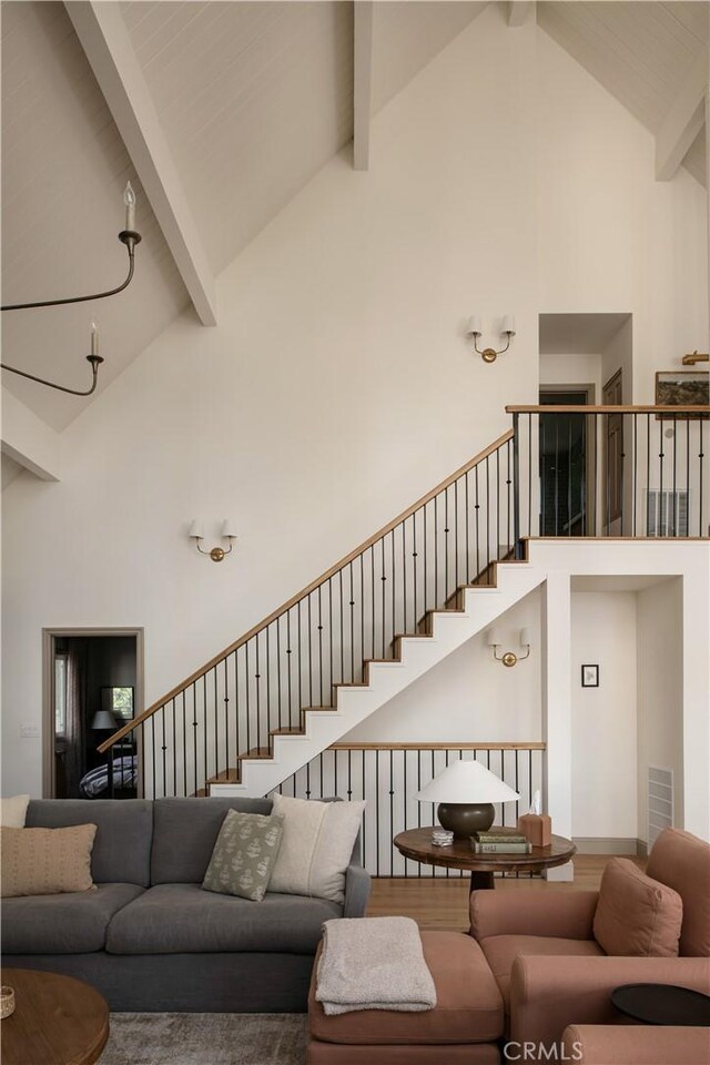 living room featuring beamed ceiling, high vaulted ceiling, visible vents, and stairway