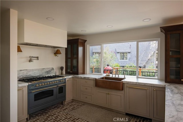 kitchen featuring range with two ovens, range hood, a sink, glass insert cabinets, and brick floor