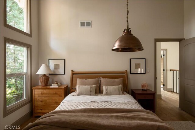 bedroom featuring multiple windows, visible vents, wood finished floors, baseboards, and a high ceiling