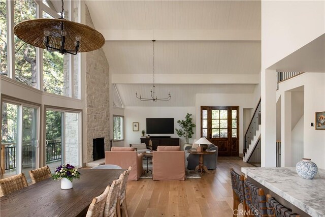 dining space with a notable chandelier, high vaulted ceiling, a stone fireplace, light wood-type flooring, and stairway