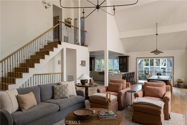 living area with a notable chandelier, high vaulted ceiling, wood finished floors, beamed ceiling, and stairway