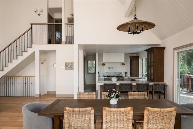 dining area with high vaulted ceiling, an inviting chandelier, wood finished floors, and stairway