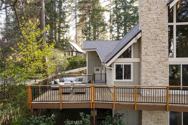 back of house with roof with shingles, a wooden deck, outdoor lounge area, and stone siding