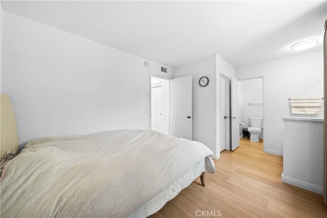 bedroom featuring baseboards, visible vents, wood finished floors, and ensuite bath