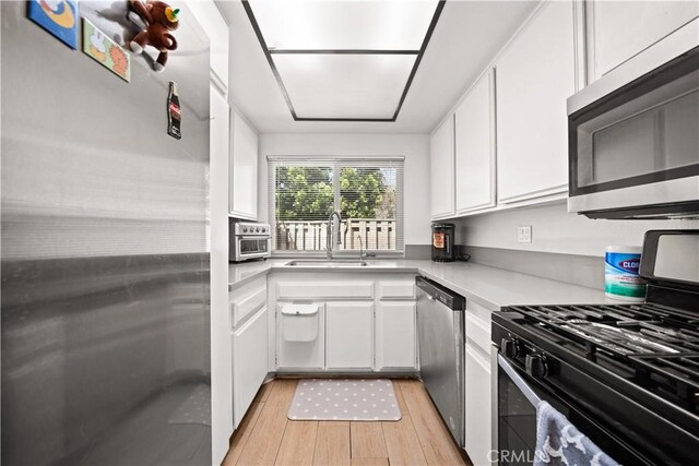 kitchen featuring light countertops, white cabinets, a sink, light wood-style flooring, and stainless steel appliances