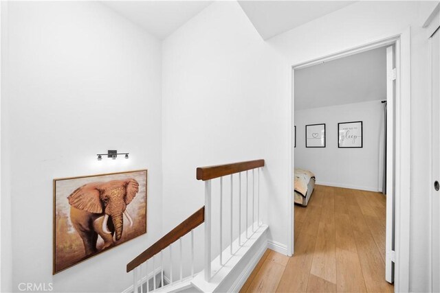 hallway featuring baseboards, light wood finished floors, and an upstairs landing