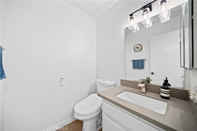 half bathroom with vanity, wood finished floors, and toilet