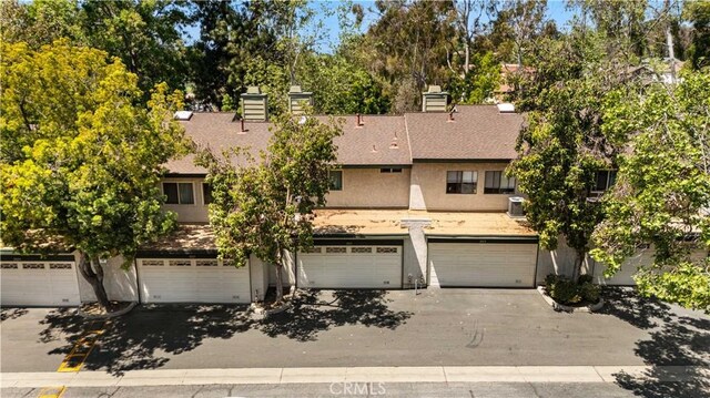 multi unit property featuring stucco siding, a chimney, a shingled roof, an attached garage, and central air condition unit