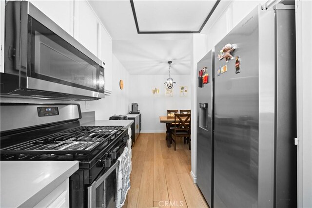 kitchen with appliances with stainless steel finishes, white cabinetry, baseboards, a notable chandelier, and light wood-style flooring