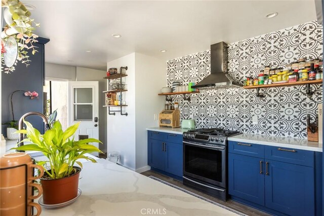 kitchen featuring open shelves, stainless steel range with gas stovetop, blue cabinetry, wall chimney exhaust hood, and backsplash