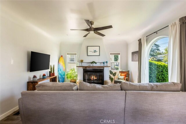 living room featuring baseboards, a glass covered fireplace, and ceiling fan