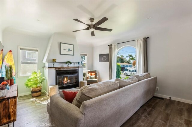 living area featuring a glass covered fireplace, baseboards, a ceiling fan, and wood finished floors