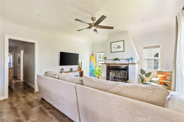living room featuring baseboards, dark wood-style flooring, ceiling fan, and a glass covered fireplace