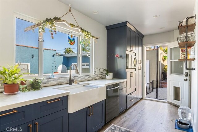 kitchen featuring appliances with stainless steel finishes, a sink, light countertops, light wood-type flooring, and backsplash