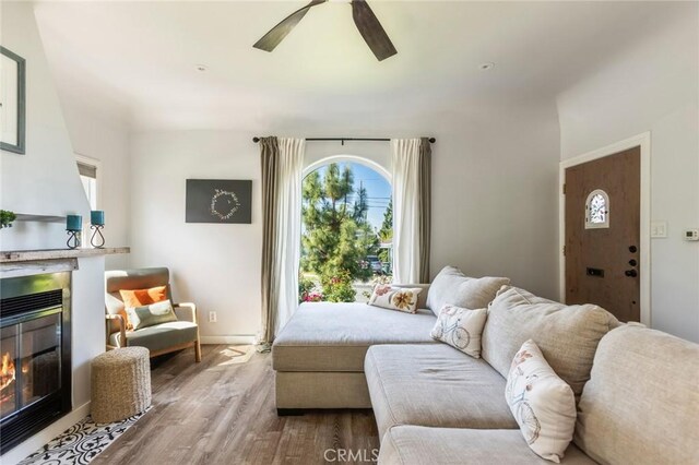 living room featuring ceiling fan, a glass covered fireplace, a wealth of natural light, and wood finished floors