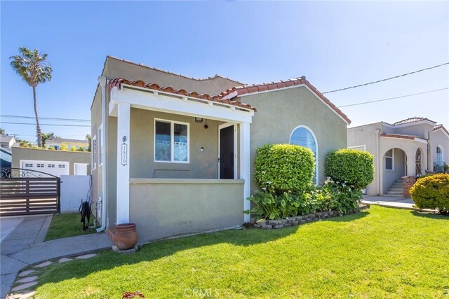 mediterranean / spanish house featuring a tile roof, a front yard, a gate, fence, and stucco siding