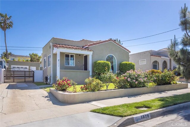view of front of property featuring a tiled roof, a gate, stucco siding, and driveway