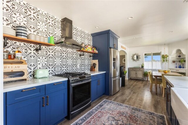 kitchen featuring open shelves, light countertops, wall chimney exhaust hood, arched walkways, and appliances with stainless steel finishes