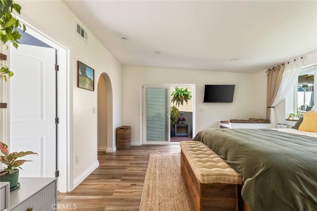 bedroom with visible vents, arched walkways, light wood-style floors, and baseboards