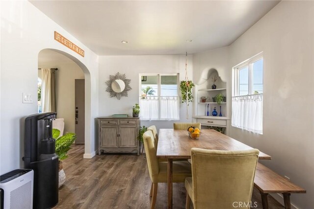 dining space with arched walkways and dark wood-type flooring