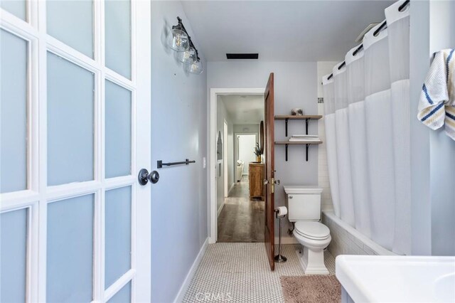 bathroom with toilet, tile patterned floors, baseboards, and shower / bath combo