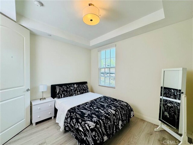 bedroom featuring a tray ceiling, baseboards, and light wood finished floors