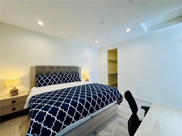 bedroom with recessed lighting, a walk in closet, and light wood-style flooring