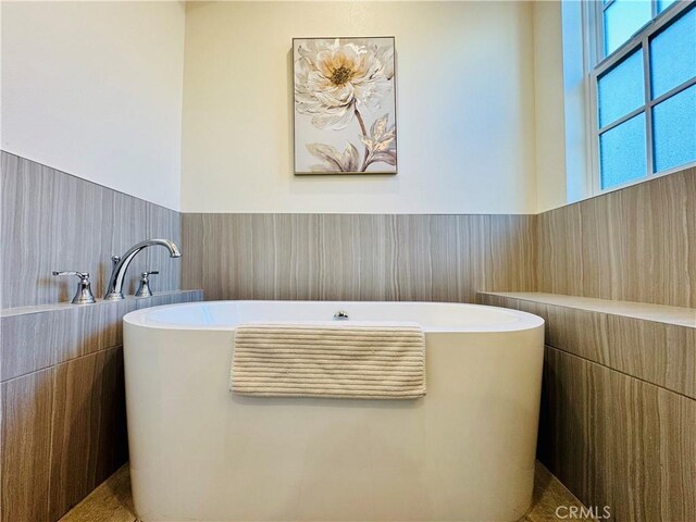 full bath with a freestanding tub and a wainscoted wall