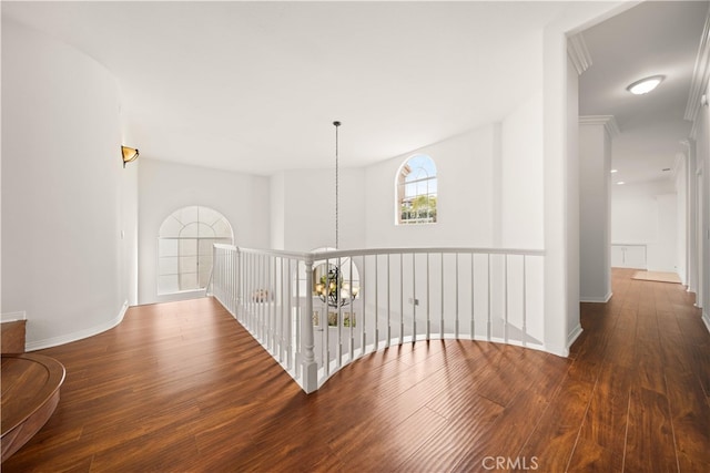 corridor featuring baseboards, wood finished floors, and a notable chandelier