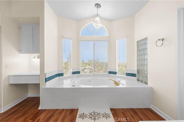 bathroom featuring baseboards, a bath, wood finished floors, and a notable chandelier