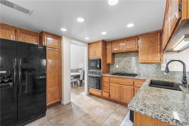 kitchen with visible vents, decorative backsplash, light stone countertops, a sink, and black appliances