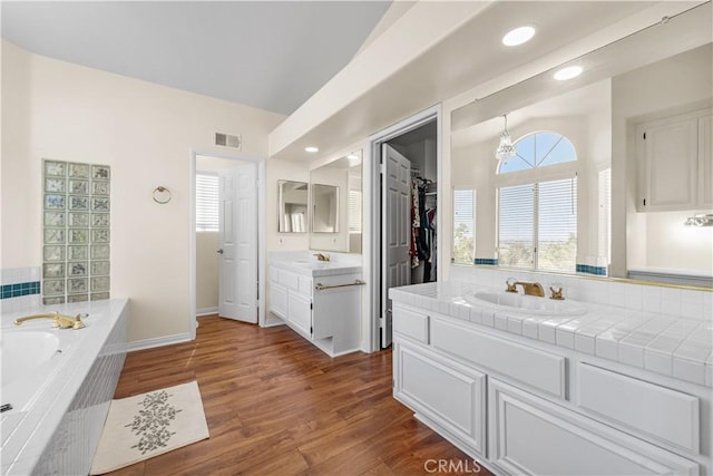 full bathroom featuring visible vents, wood finished floors, a bath, two vanities, and a sink