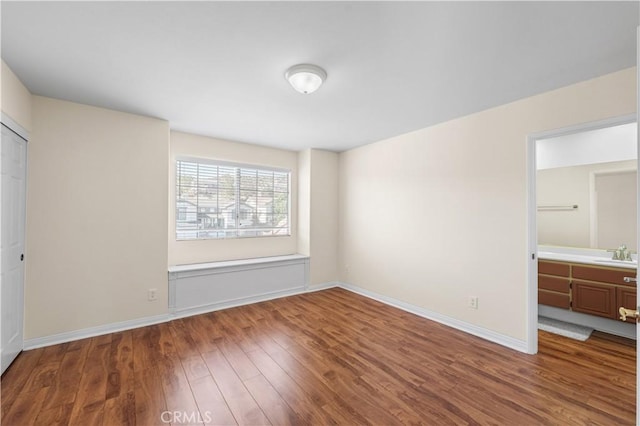unfurnished bedroom featuring a sink, baseboards, and wood finished floors