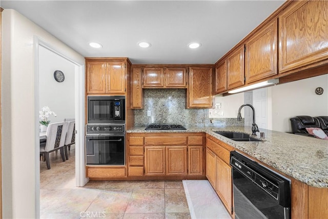 kitchen featuring decorative backsplash, brown cabinetry, a sink, light stone counters, and black appliances