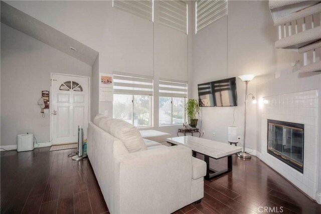 living area with baseboards, a tiled fireplace, dark wood-type flooring, and a towering ceiling
