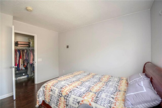 bedroom with baseboards, a closet, dark wood finished floors, and a spacious closet