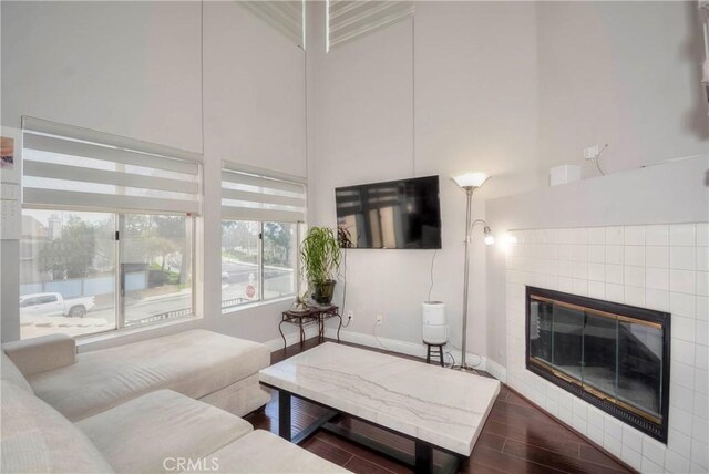 living room with baseboards, a tile fireplace, wood finished floors, and a towering ceiling
