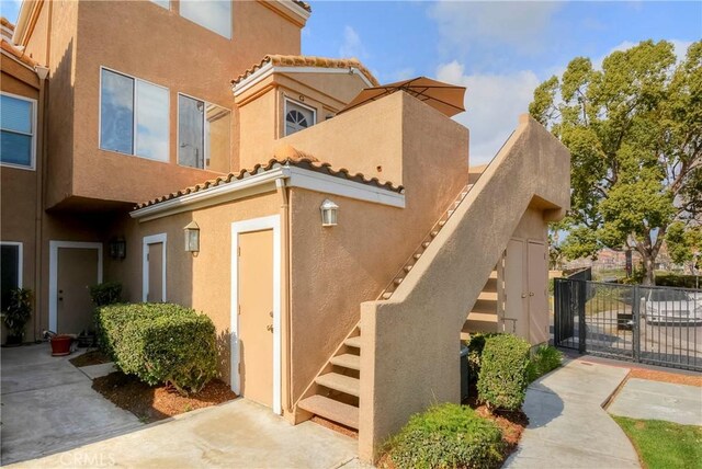 view of side of home featuring a gate, stucco siding, a tiled roof, and fence