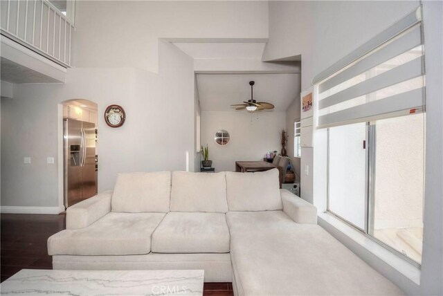 living room featuring ceiling fan, arched walkways, baseboards, wood finished floors, and a towering ceiling
