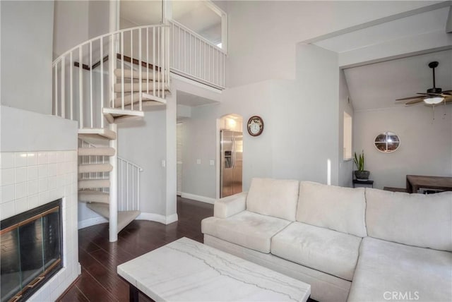 living room featuring a towering ceiling, baseboards, ceiling fan, dark wood-style floors, and stairway