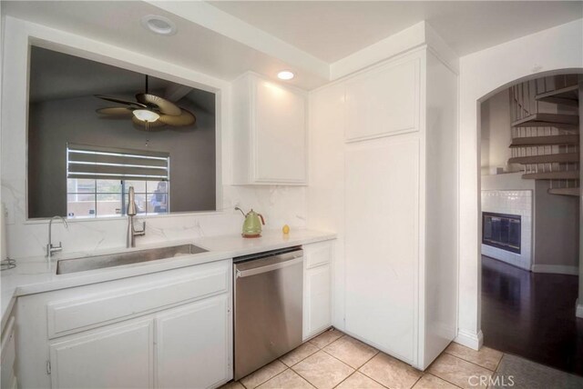 kitchen featuring a ceiling fan, dishwasher, a sink, white cabinets, and a glass covered fireplace
