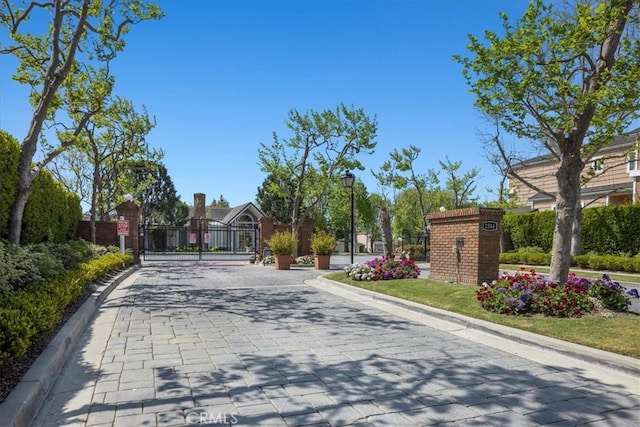 view of street with a gate, a gated entry, curbs, and street lights