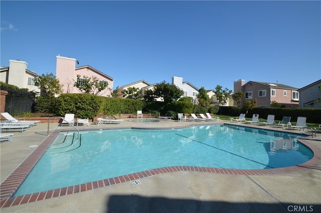 community pool featuring fence, a patio, and a residential view